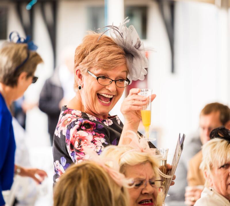 A hospitality guest at Sedgefield Racecourse who is happily toasting her drink.